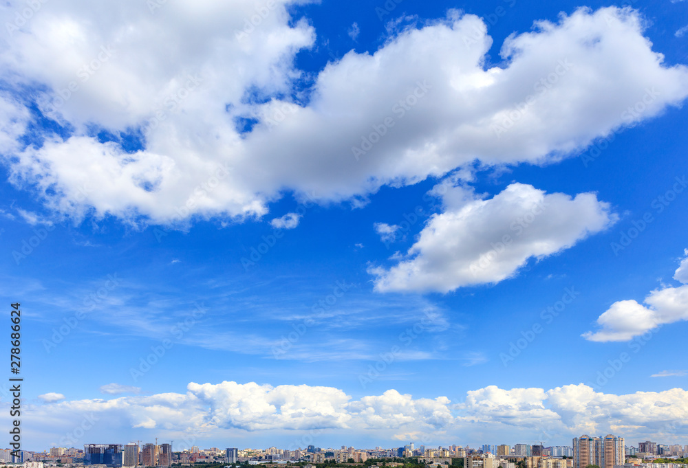Large white clouds float in the blue sky above the city skyline.