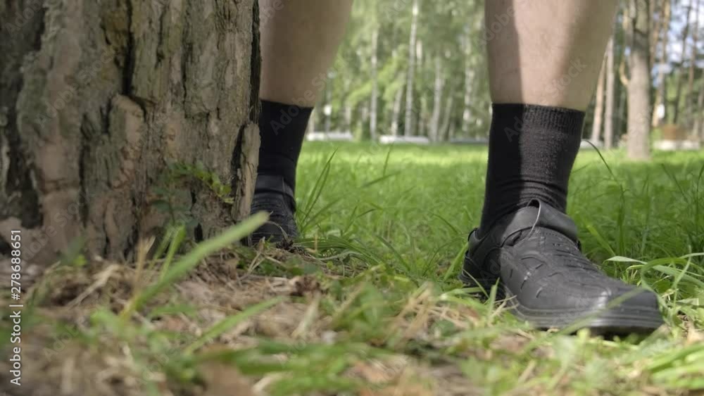 men's feet in shoes treading near tree. man is hiding behind tree in park. men's feet in shoes treading near tree. man is hiding behind tree in park.