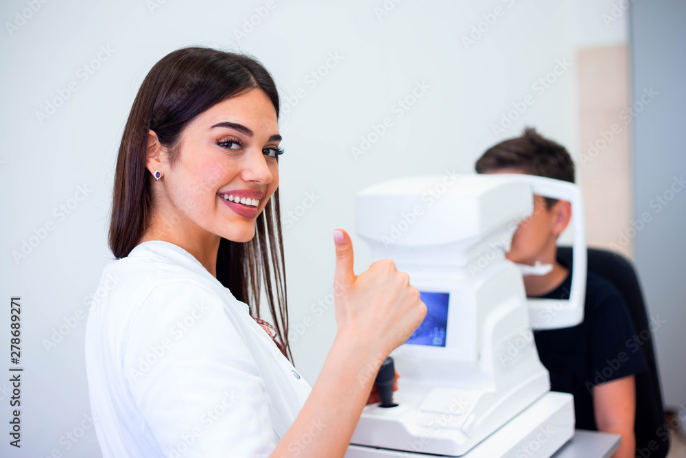 Female oculist using machine for checking eye sight in clinic. Little boy looking at equipment and doctor testing eye pupil in optical store. Concept of eye care and health. Female oculist using machine for checking eye sight in clinic. Little boy looking at equipment and doctor testing eye pupil in optical store. Concept of eye care and health.