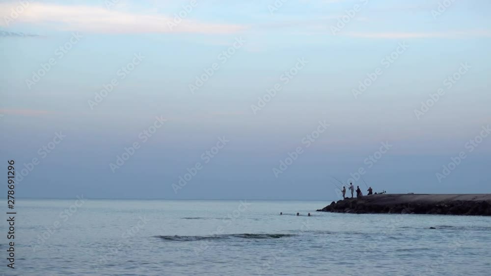 4K view of evening sea coast. Silhouettes of fishermen with fishing poles and people floating in the sea. 4K view of evening sea coast. Silhouettes of fishermen with fishing poles and people floating in the sea.