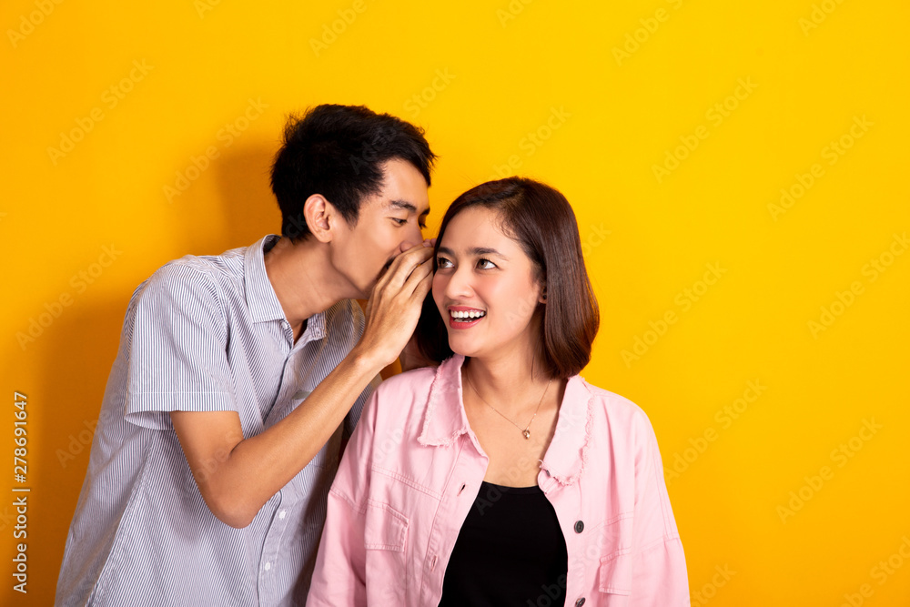 man whispering to a woman about gossip, woman looked shocked shoot over yellow background man whispering to a woman about gossip, woman looked shocked shoot over yellow background