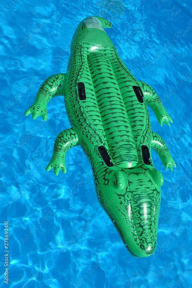 A green crocodile plastic pool float on a sandy beach Stock Photo
