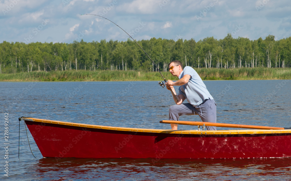 a man in a boat, in the center of the lake, throws a fishing rod to catch a big fish, against the backdrop of a beautiful landscape