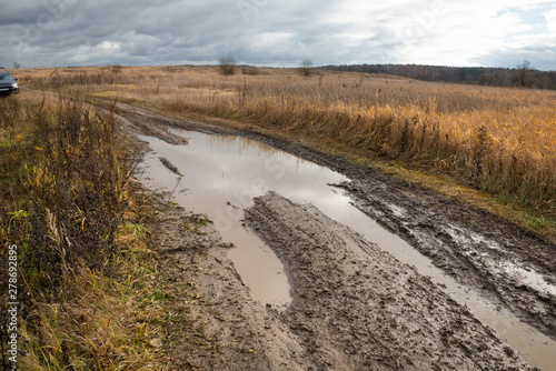 Country road rut with puddles through agricultural field