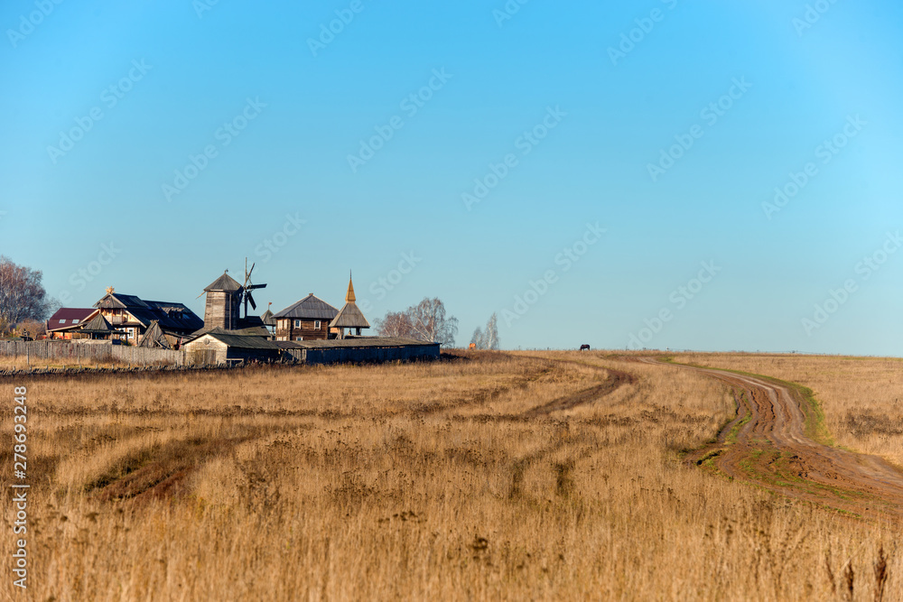 Fototapeta premium Autumn landscape. The road through the field to the entrance gate and the wooden wall of the Slavic Kremlin