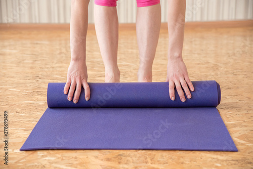 Slender woman unfolds purple mat for gymnastics or yoga in the gym