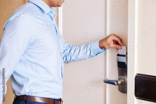 Close-up of young businessman in blue shirt opening the door of hotel room with card key and check in © DragonImages