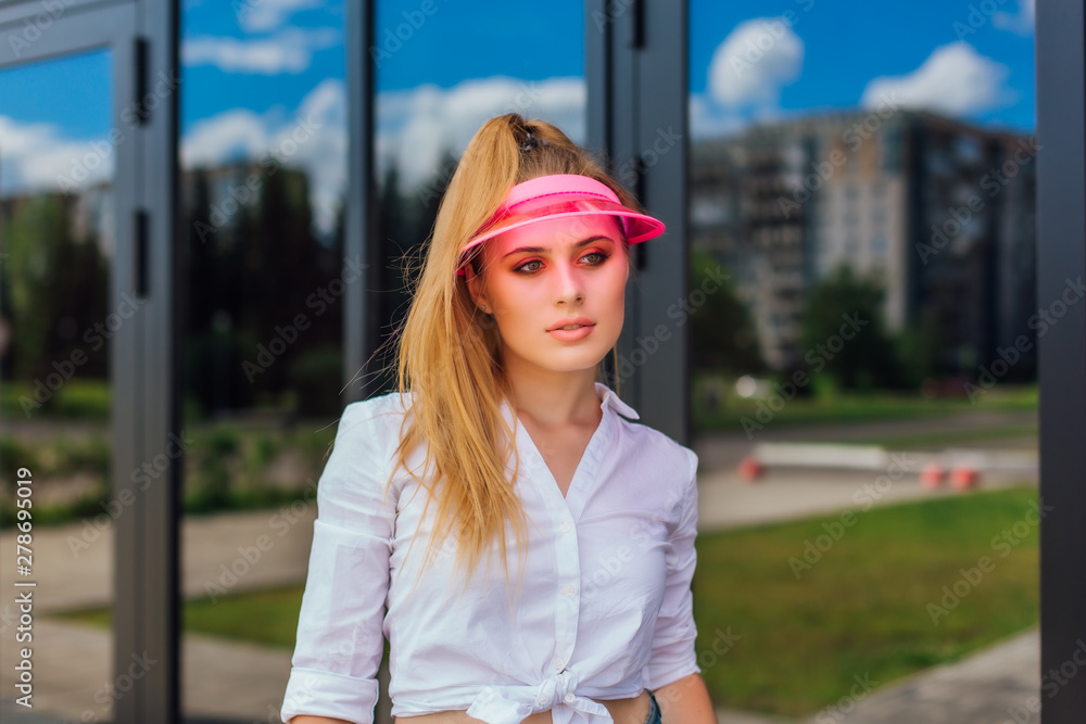 Portrait of an emotional girl in a pink cap visor and protective gloves for rollerblades and skateboarding.