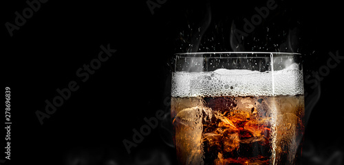Soft drink glass with ice splash on cool smoke background. Cola glass with summer refreshment. photo