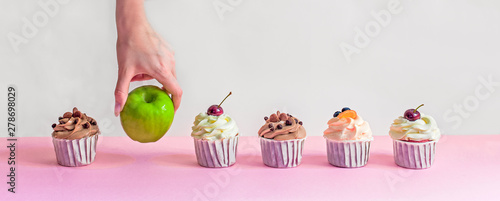apple among cupcakes, healthy food choices, female hand picks green apple, fatty sweet food, diet, weight loss