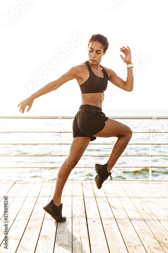 Image of athletic young woman in sportive clothes doing workout by seaside in morning © Drobot Dean