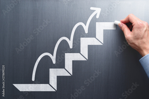Steps to succeed in business. Businessman drawing steps and arrow on chalkboard. photo