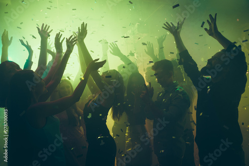 Close up photo of many party people dancing clubbing green lights confetti flying everywhere nightclub hands raised up shiny formal-wear