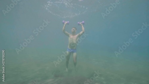 Wallpaper Mural Athletic man does sport exercise with dumbbells underwater stands on ocean floor. Torontodigital.ca
