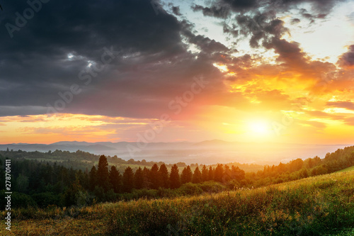 Sunset landscape in mountains with cloudy sky above forest hills.