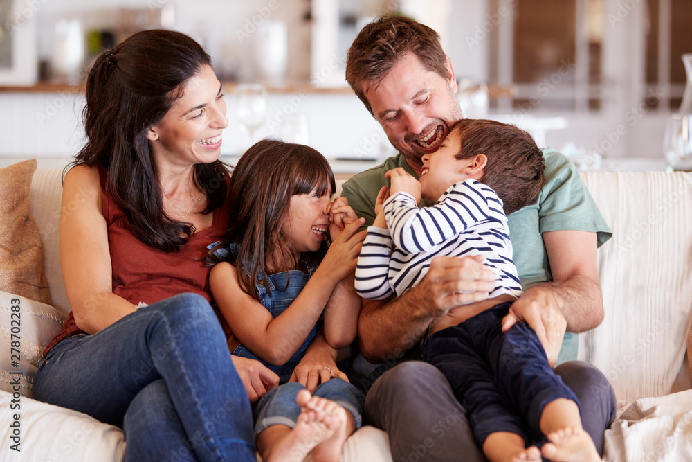 Mid adult white couple and their two young children sitting on a sofa at home smiling at each other Mid adult white couple and their two young children sitting on a sofa at home smiling at each other