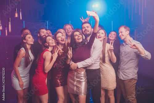 Portrait of nice well-dressed chic glamorous attractive shine stylish cheerful cheery positive glad excited ladies and guys having fun taking selfie showing v-sign at luxury fogged nightclub indoors