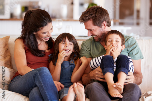 Mid adult white couple and their two young children sitting on a sofa at home smiling at each other