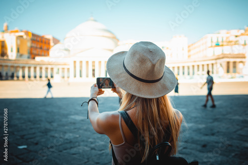 Europe travel summer tourism holiday vacation background - young attractive Caucasian smiling beautiful blonde girl face with hat mobile cell phone and using backpack in hand taking selfie photo