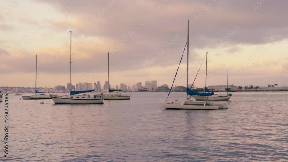 Sailboats on water in San Diego California harbor during pink cloudy sunset, Coronado island with navy buildings and downtown in the background Sailboats on water in San Diego California harbor during pink cloudy sunset, Coronado island with navy buildings and downtown in the background