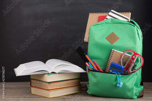 Education concept - school backpack with books and other supplies, blackboard background photo