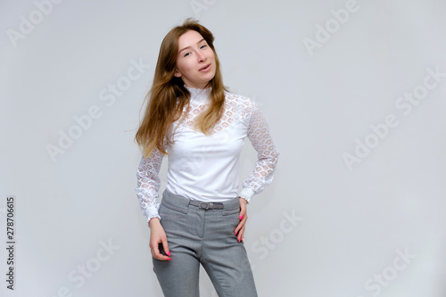 Portrait of a knee-high young pretty brunette girl woman with beautiful long hair on a white background in a white jacket and gray pants. He talks, shows his hands with emotions in various poses.