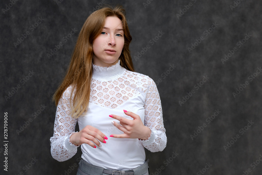 Portrait to the waist of a young pretty brunette girl woman with beautiful long hair on a gray background in a white jacket. He talks, smiles, shows his hands with emotions in various poses. Portrait to the waist of a young pretty brunette girl woman with beautiful long hair on a gray background in a white jacket. He talks, smiles, shows his hands with emotions in various poses.