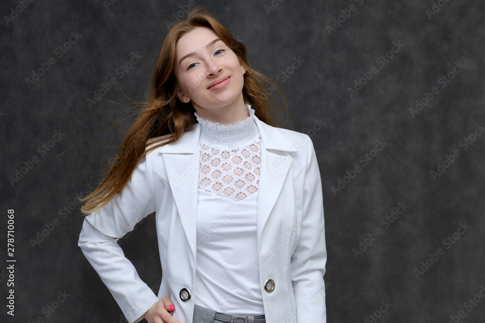 Portrait to the waist of a young pretty brunette girl woman with beautiful long hair on a gray background in a white jacket. He talks, smiles, shows his hands with emotions in various poses. Portrait to the waist of a young pretty brunette girl woman with beautiful long hair on a gray background in a white jacket. He talks, smiles, shows his hands with emotions in various poses.