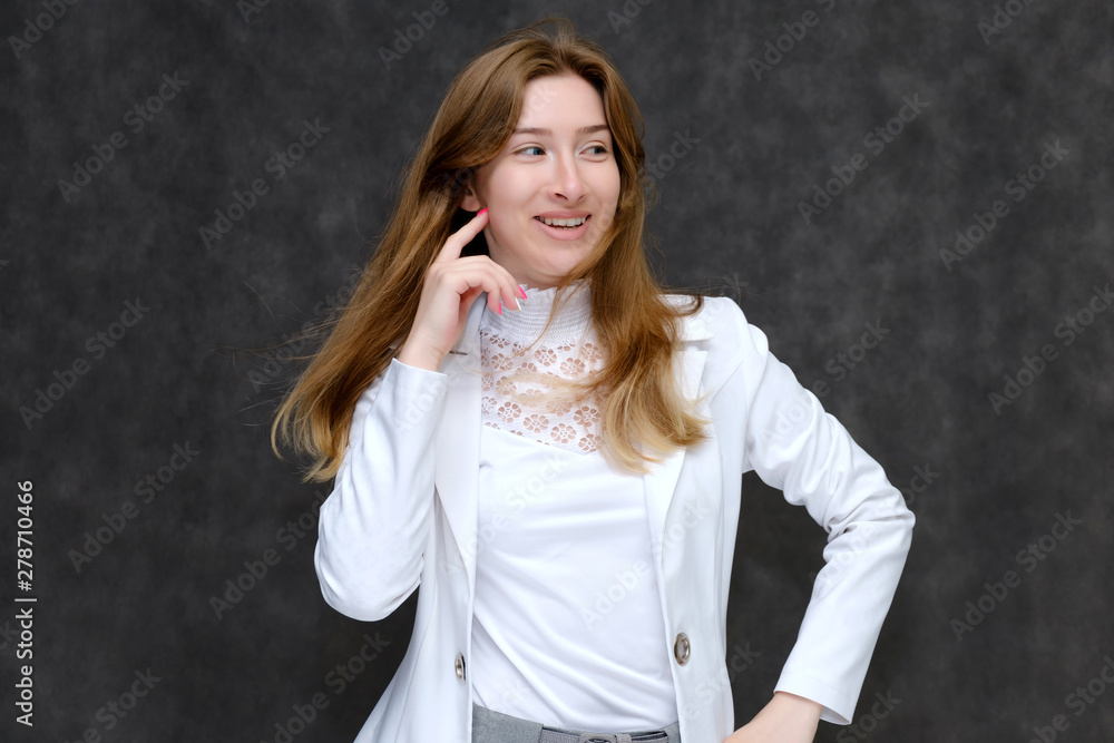 Portrait to the waist of a young pretty brunette girl woman with beautiful long hair on a gray background in a white jacket. He talks, smiles, shows his hands with emotions in various poses. Portrait to the waist of a young pretty brunette girl woman with beautiful long hair on a gray background in a white jacket. He talks, smiles, shows his hands with emotions in various poses.
