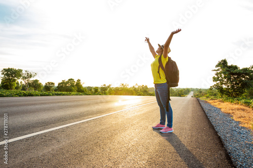 Women tourists carrying a backpack that holds his hands up to the sky on the highway with the golden light of the sun, Happy mood from tourism.