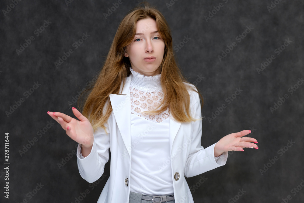 Portrait to the waist of a young pretty brunette girl woman with beautiful long hair on a gray background in a white jacket. He talks, smiles, shows his hands with emotions in various poses. Portrait to the waist of a young pretty brunette girl woman with beautiful long hair on a gray background in a white jacket. He talks, smiles, shows his hands with emotions in various poses.