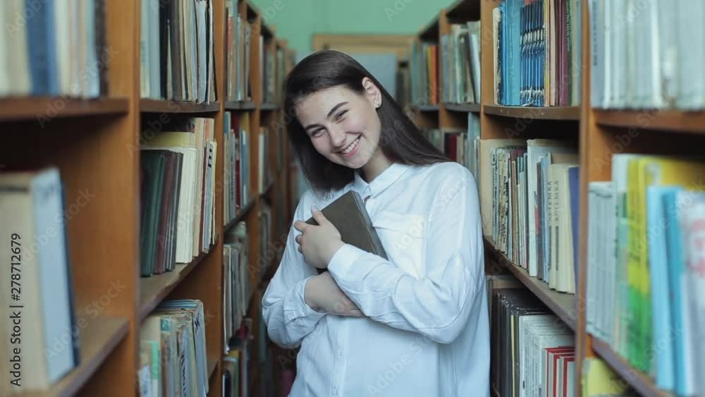 Smart looking and beautiful young girl in white shirt and glasses in collage school library selecting book to read Smart looking and beautiful young girl in white shirt and glasses in collage school library selecting book to read