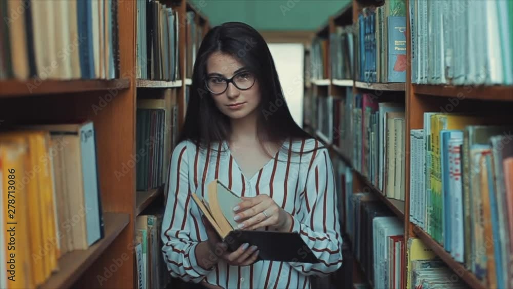 Young pretty woman with glasses in the library holding a book in her hand, leafing through the pages. Young pretty woman with glasses in the library holding a book in her hand, leafing through the pages.