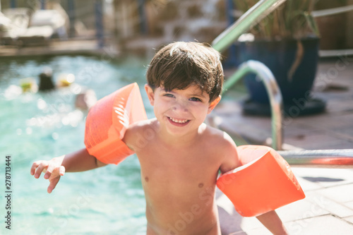 little three years old kid boy with arms float in swimming pool ready to go to water