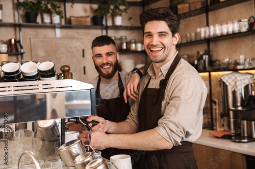 Group of cheerful men baristas wearing aprons photo