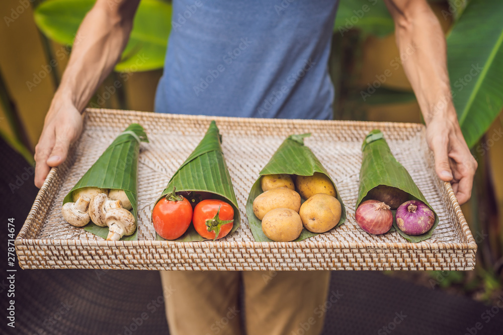 Eco-friendly product packaging concept. Vegetables wrapped in a banana leaf, as an alternative to a plastic bag. Zero waste concept. Alternative packaging - obrazy, fototapety, plakaty 