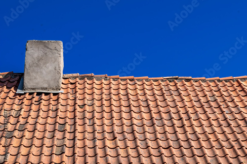 Traditional old Tile Roofing made of clay. Natural roofing material. Clay tiles with chimney on the background of blue sky. © Konstantin