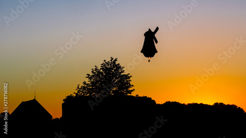 On a hot June evening in the Eastern Netherlands an air balloon shaped like a traditional Dutch windmill is flying across the sky when the sun is setting. Ballooning is popular in The Netherlands