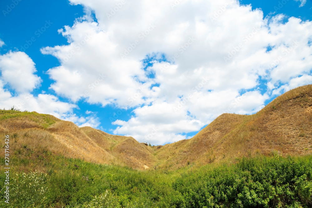 Erosion of land. Landscape with a picturesque ravine on a background of bright blue sky with clouds on a summer warm sunny day in nature outdoors Erosion of land. Landscape with a picturesque ravine on a background of bright blue sky with clouds on a summer warm sunny day in nature outdoors