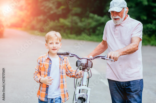 Senior man grandfather and grandson talking while walking with bicycle in the park. Family, generation, safety and people concept.