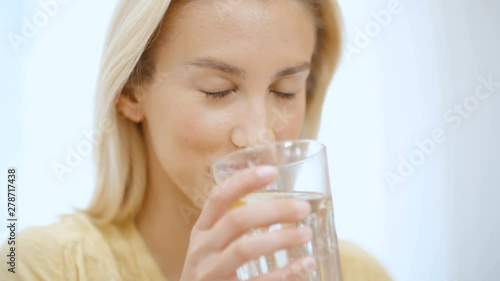 Portrait of young woman in pajama holding water while sitting on a bed.