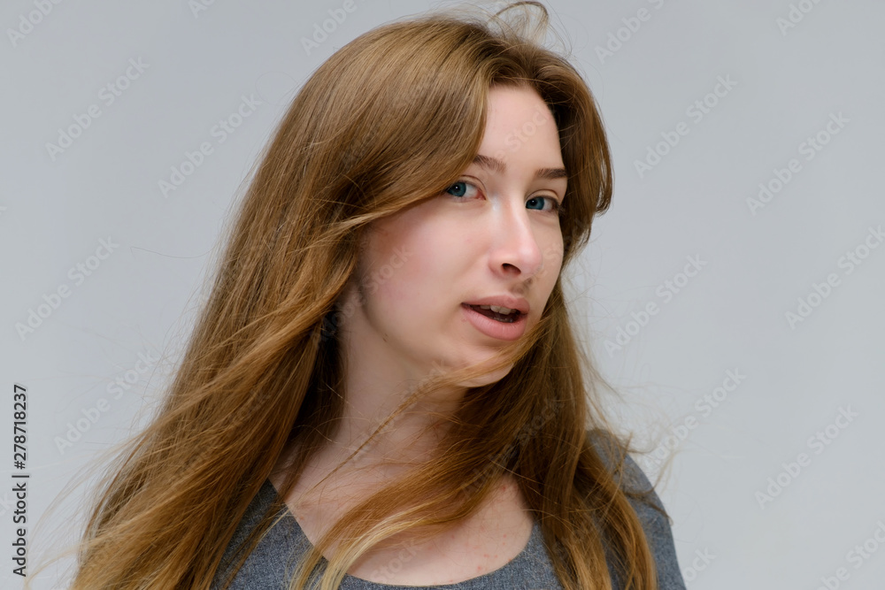 Close-up portrait of a young pretty brunette girl woman with beautiful long hair on a white background in a gray dress. He talks, smiles, shows his hands with emotions in various poses. Close-up portrait of a young pretty brunette girl woman with beautiful long hair on a white background in a gray dress. He talks, smiles, shows his hands with emotions in various poses.