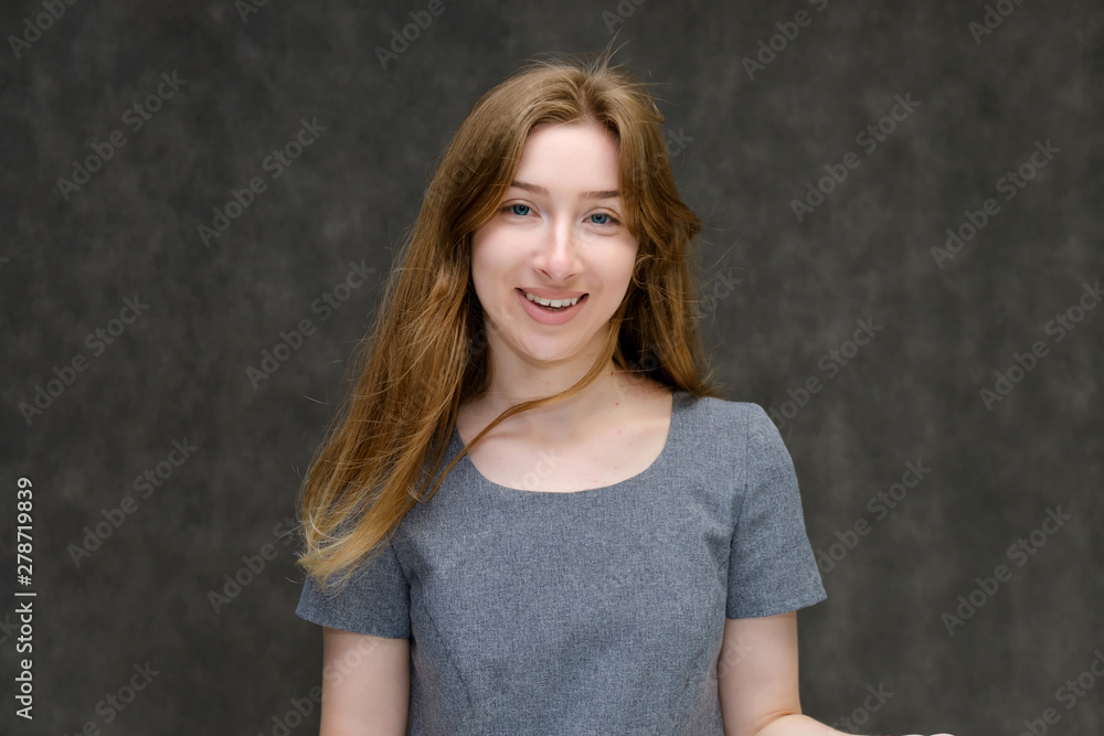 Portrait below the chest of a young pretty brunette girl woman with beautiful long hair on a gray background in a gray dress. He talks, smiles, shows his hands with emotions in various poses. Portrait below the chest of a young pretty brunette girl woman with beautiful long hair on a gray background in a gray dress. He talks, smiles, shows his hands with emotions in various poses.