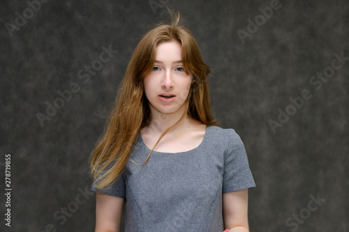 Portrait below the chest of a young pretty brunette girl woman with beautiful long hair on a gray background in a gray dress. He talks, smiles, shows his hands with emotions in various poses.