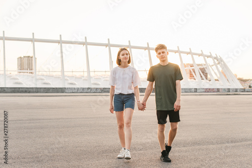 Beautiful lovely couple strolls by holding hands in the background of the city landscape,looking into the camera and smiling.Portrait stylish couple of casual clothes in the background of the city