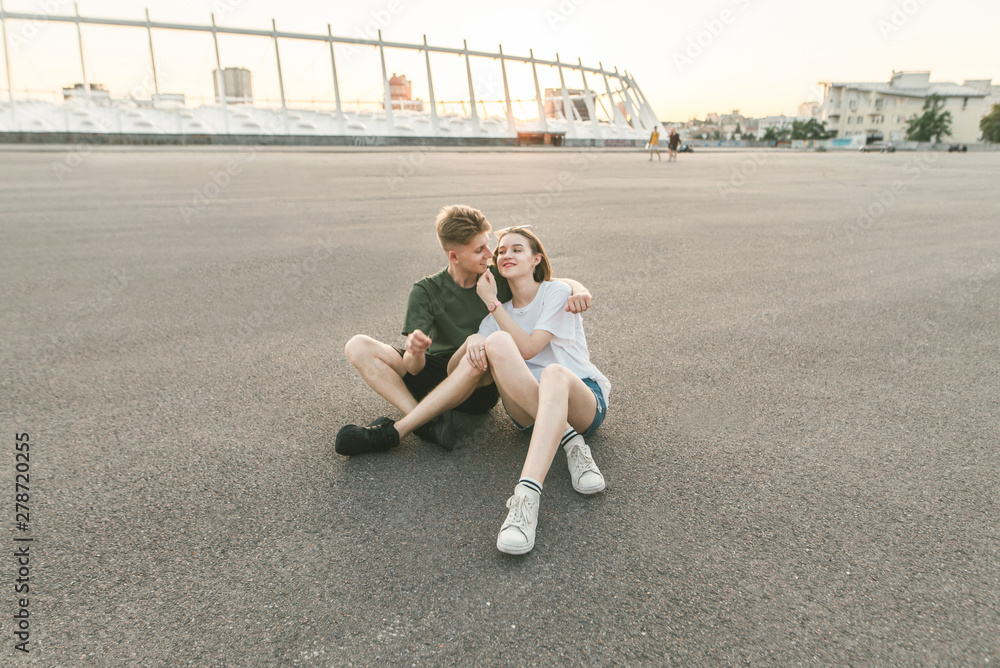 Φωτογραφία Beautiful young couple sitting sitting on the asphalt, background of an incredible sunset, looking into the camera and smiling