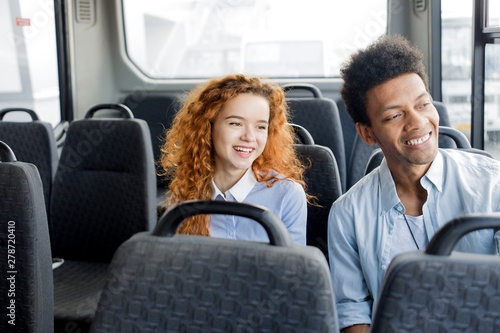 African guy with red-haired girl sitting on the passenger seat ride the bus around the city