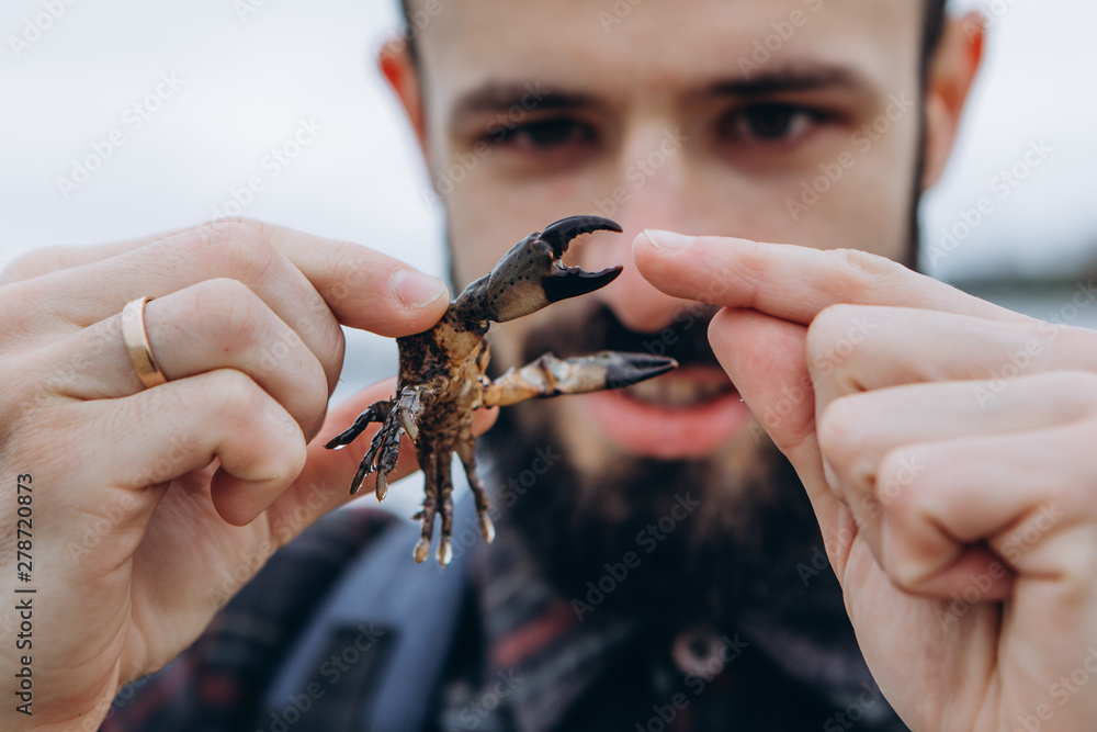 A cool picture of a man who holds a small crab in his arms while walking along the sea in cloudy cold weather A cool picture of a man who holds a small crab in his arms while walking along the sea in cloudy cold weather