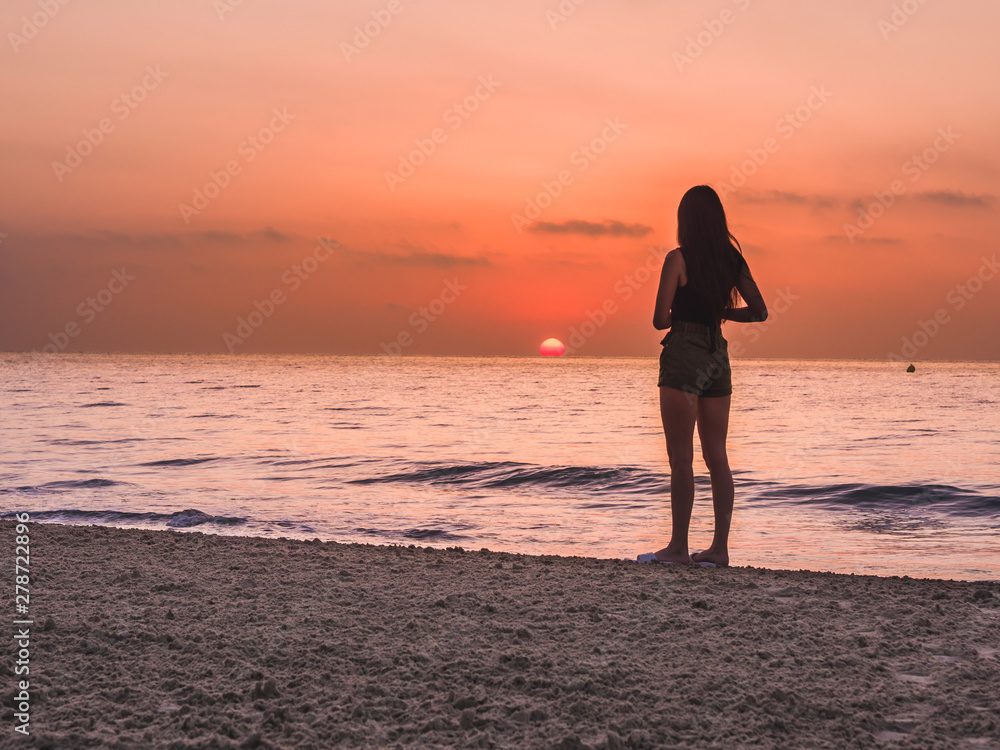 Fototapeta premium young girl on the beach watching the sunset