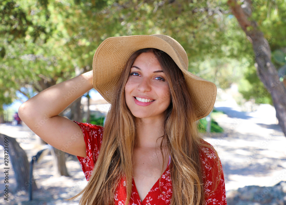 Portrait of a beautiful smiling girl wearing red dress and straw hat looking at camera